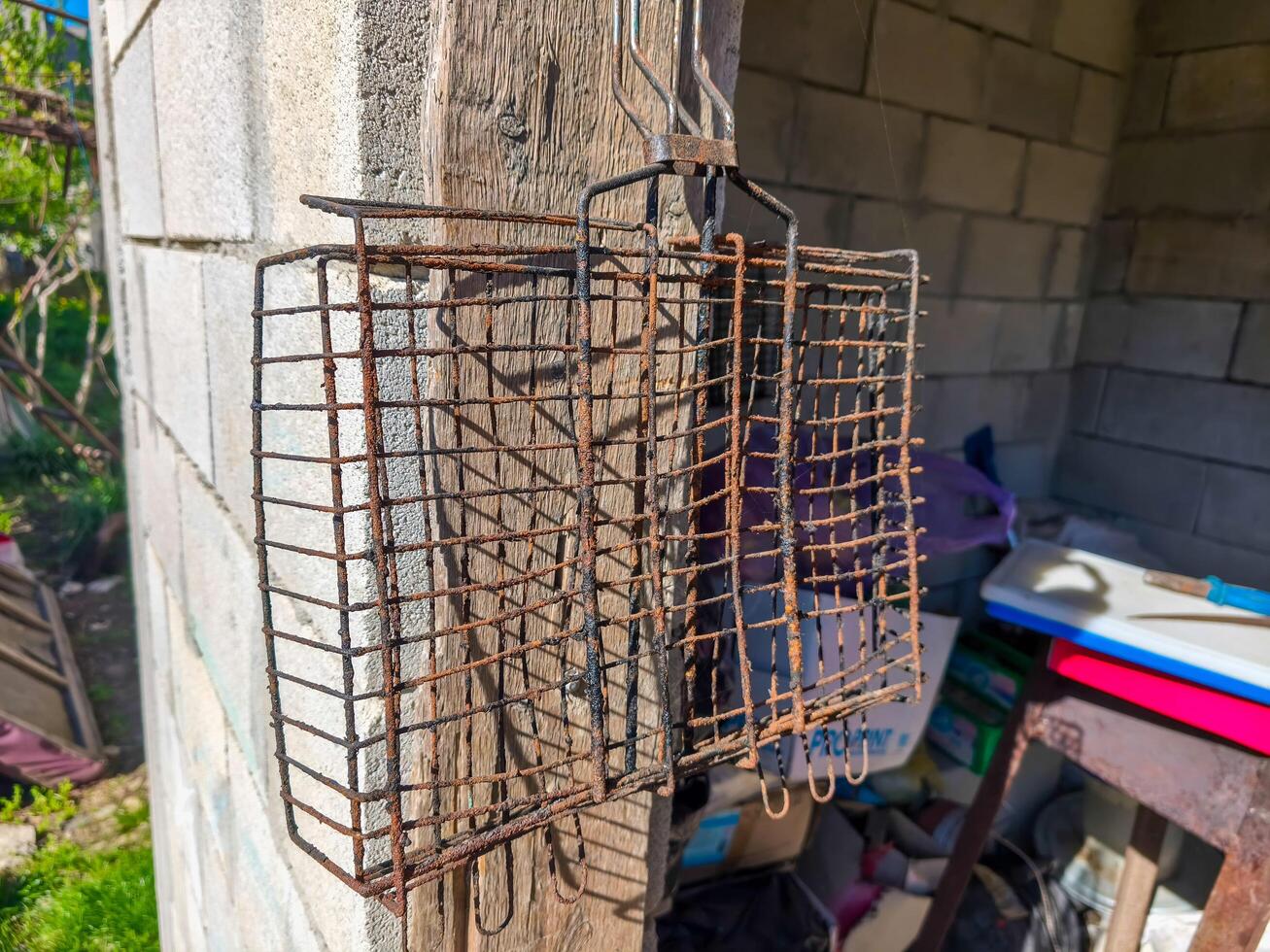 A rusty metal cage is hanging from a wall. The cage is old and has a lot of rust on it. The cage is hanging from a wooden beam photo