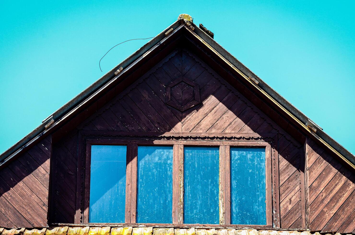 A house with a slanted roof and a window with three panes. The window is dirty and the roof is brown photo