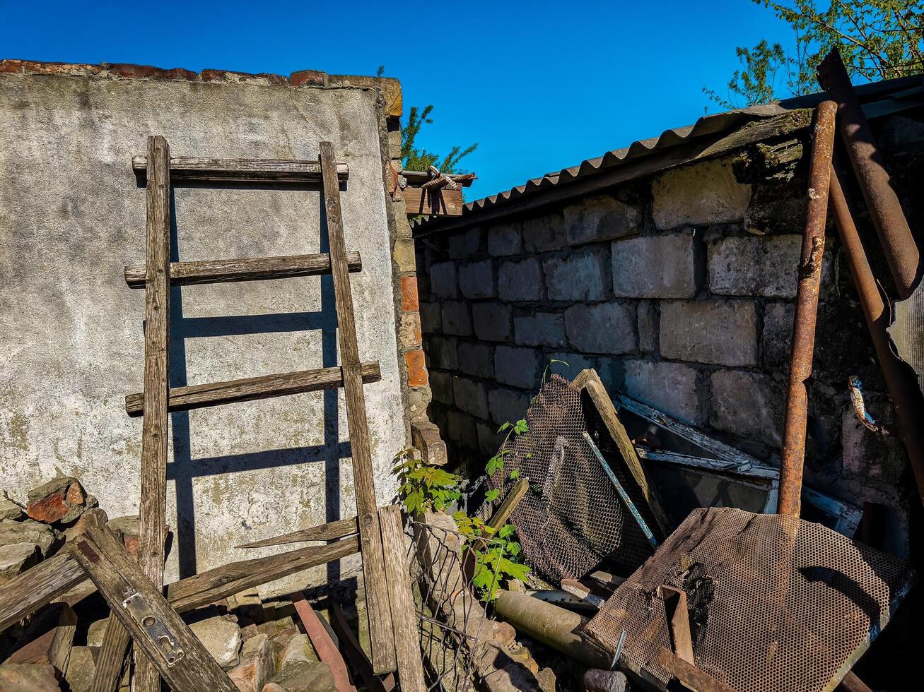 A wooden ladder leaning against a brick wall. The ladder is old and rusted. The wall is made of bricks and has a metal roof. The scene is somewhat abandoned and gives off a feeling of neglect photo