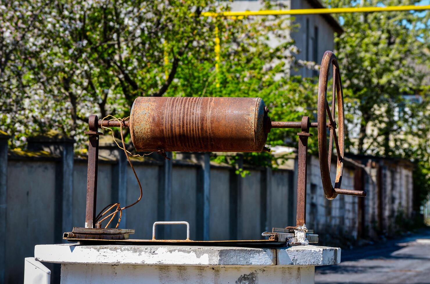A rusty old metal object with a chain wrapped around it. The chain is attached to a metal rod. The object is sitting on a cement block. The scene is quiet and peaceful photo