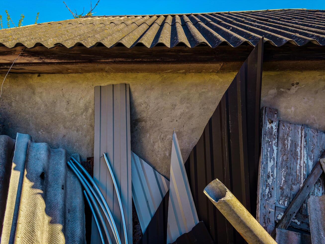 A pile of roofing materials, including shingles and metal, are stacked against a wall photo