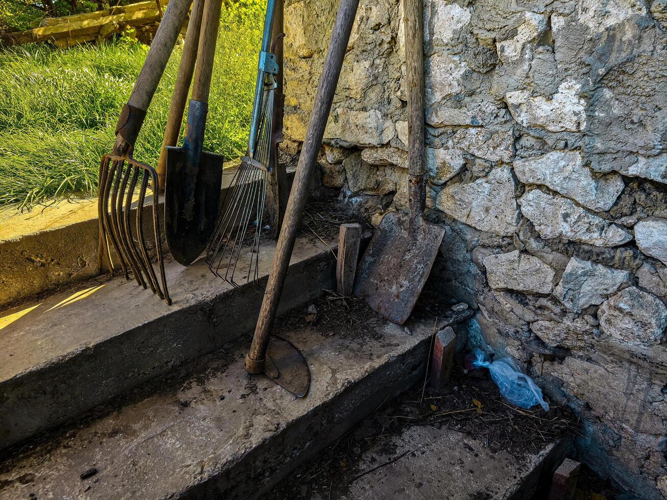 A pile of tools including a shovel, a rake, and a pitchfork are on a set of steps photo