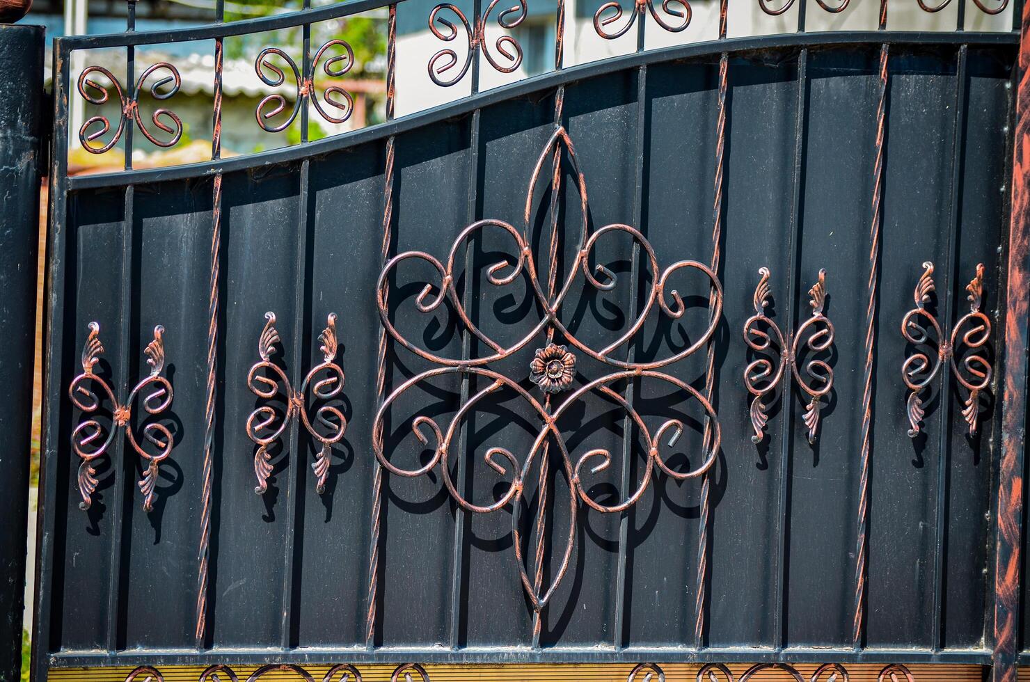A wrought iron gate with a flower design on it. The gate is black and has a gold trim photo