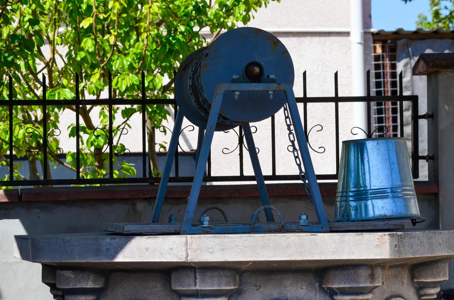 A rusty metal object is sitting on a ledge next to a bucket. The object appears to be a pulley or a crank, and the bucket is made of metal. The scene has a somewhat industrial or mechanical feel photo