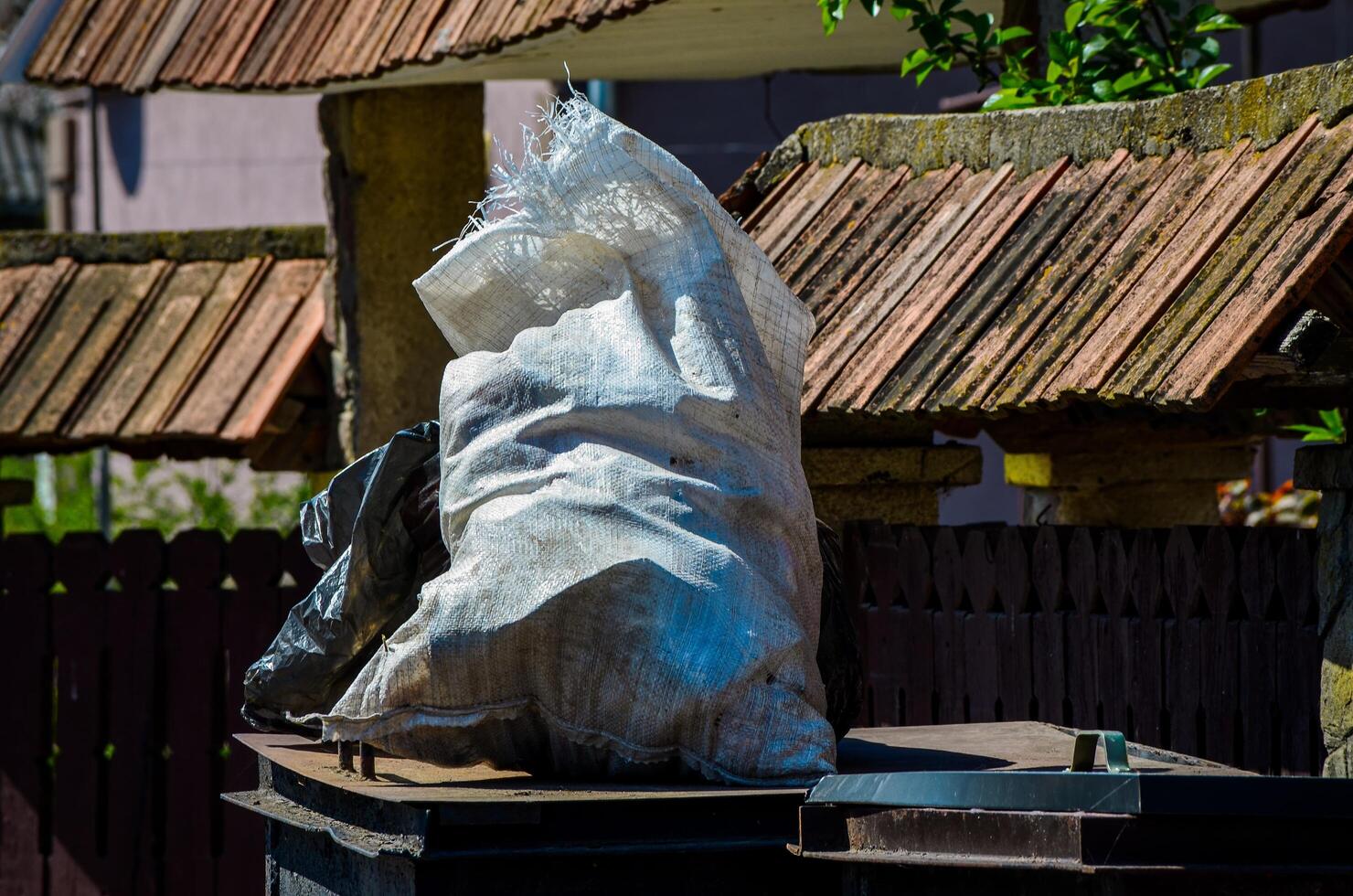 A white bag is on top of a trash can. The bag is full of trash and is covered in plastic photo