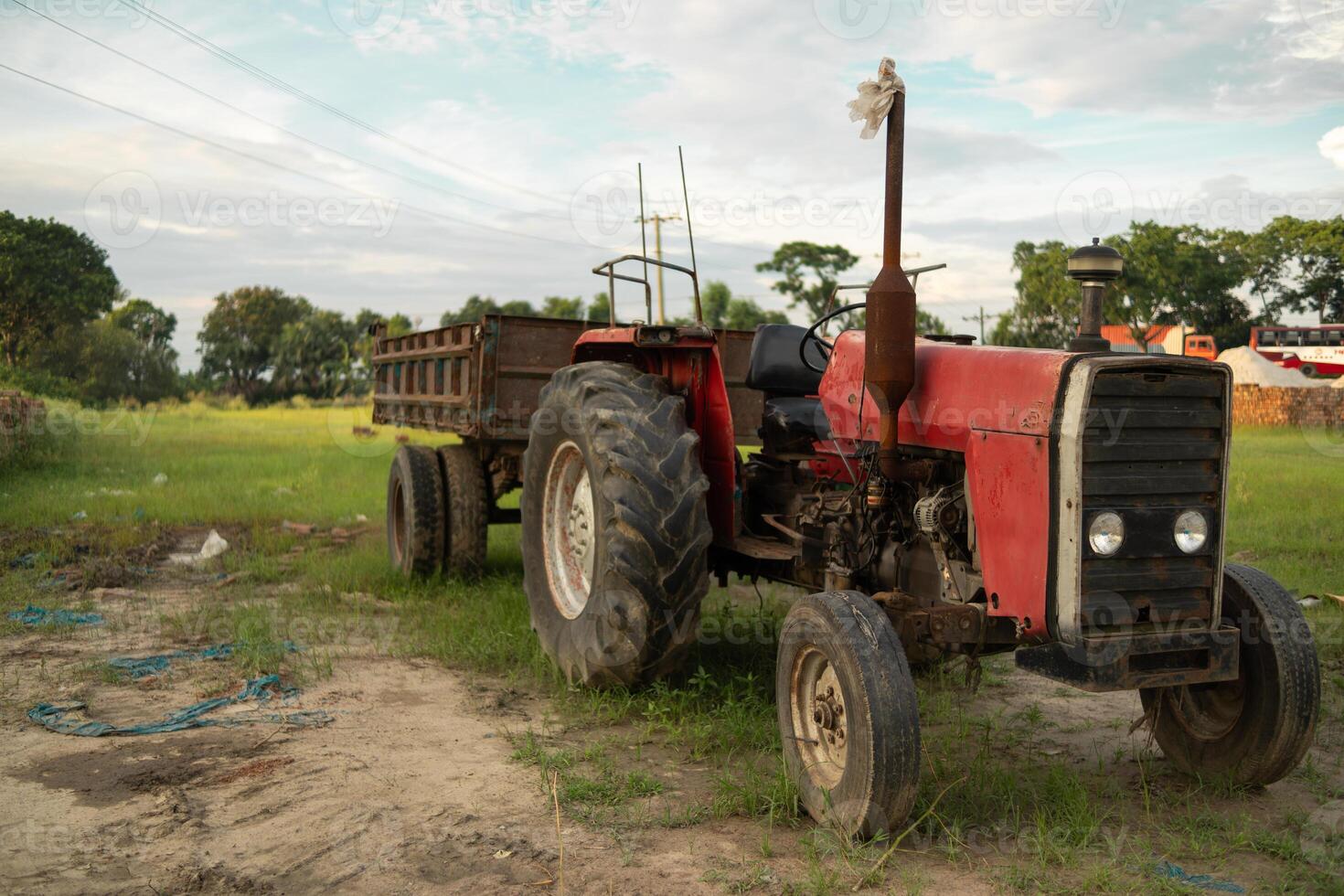 A red tractor with a trailer parked in a field photo