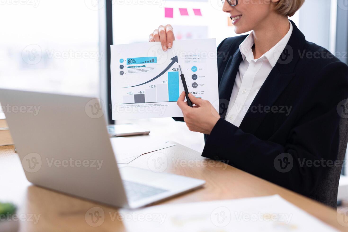 Business professional displaying economic data during meeting using printed chart, laptop on desk photo