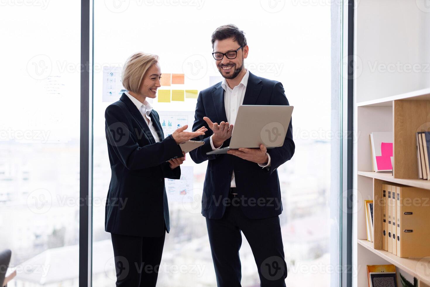 Two professionals collaborating in office environment, sharing ideas and analyzing data using laptop photo