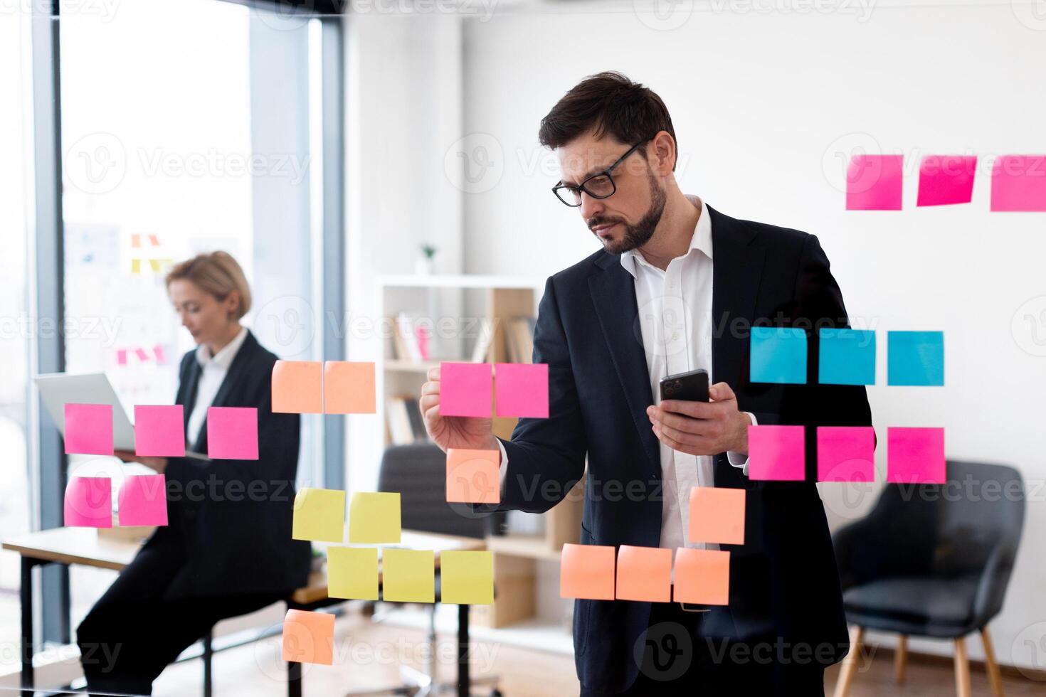 Corporate employees collaborating using glass board with colorful notes in professional workspace setting. photo