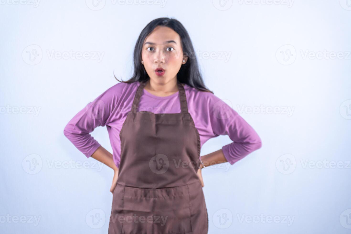 A surprised young Asian woman in a purple shirt and brown apron stands with hands on hips, eyes wide. photo