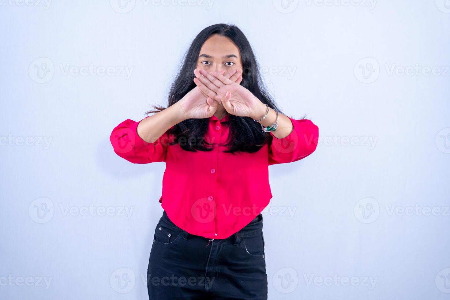 A woman in a red shirt stands with her hands crossed in front of her mouth, signaling silence or refusal to speak. photo
