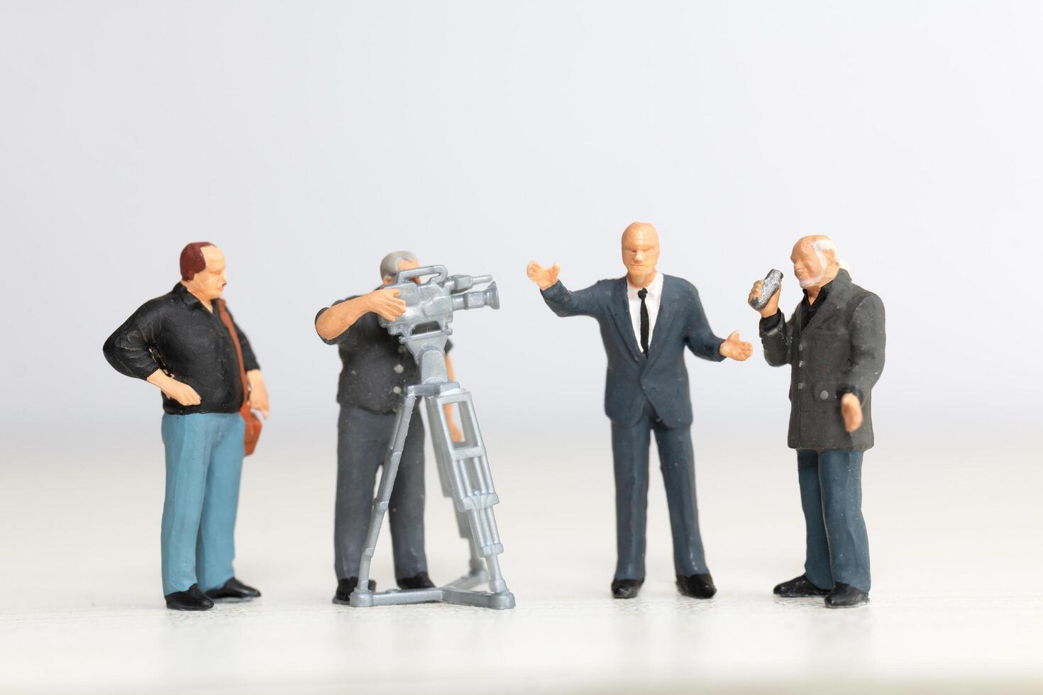 Miniature figure of a male journalist interviewing a businessman, with a cameraman recording photo