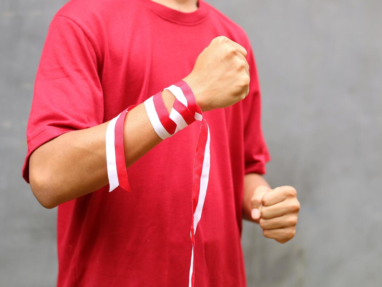 Hand with clenched fist wearing red and white ribbon on gray background during Indonesia's independence day celebration, copy space photo