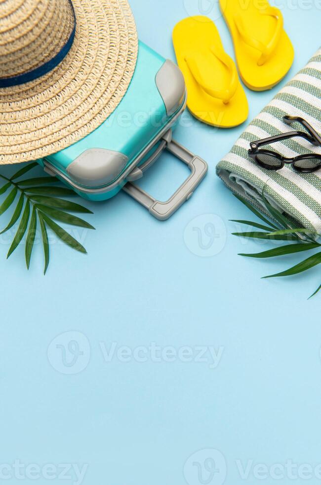 Suitcase, beach towel, flip flops, sunglasses and a straw hat suggesting summer vacation travel photo