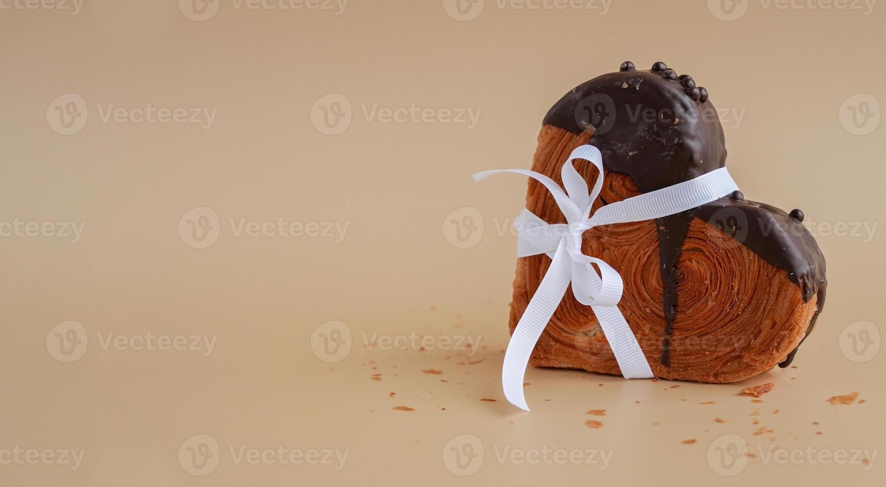 Present gift tied bow holiday Valentine's Day birthday celebration Heart shaped dark chocolate croissant on beige background with copy space. Puff pastry new trendy sweet dessert bakery. Creamy dough experiment photo