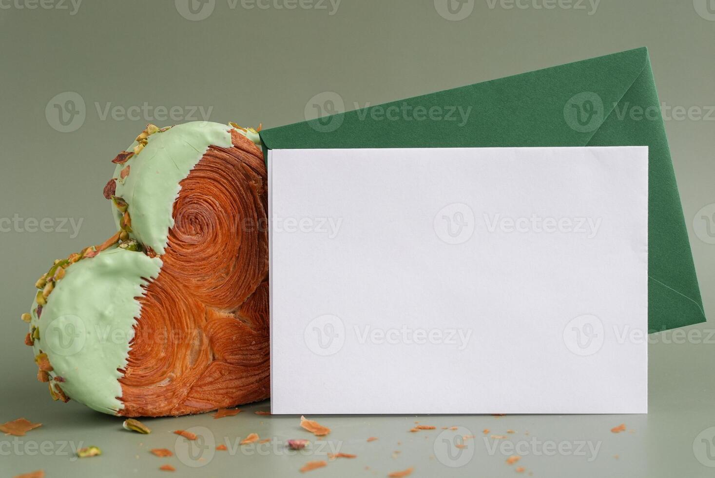 Empty template paper note with envelope greeting card mock up. Heart shaped pistachio croissant on green background with copy space. Puff pastry new trendy sweet dessert bakery. Creamy dough experiment photo