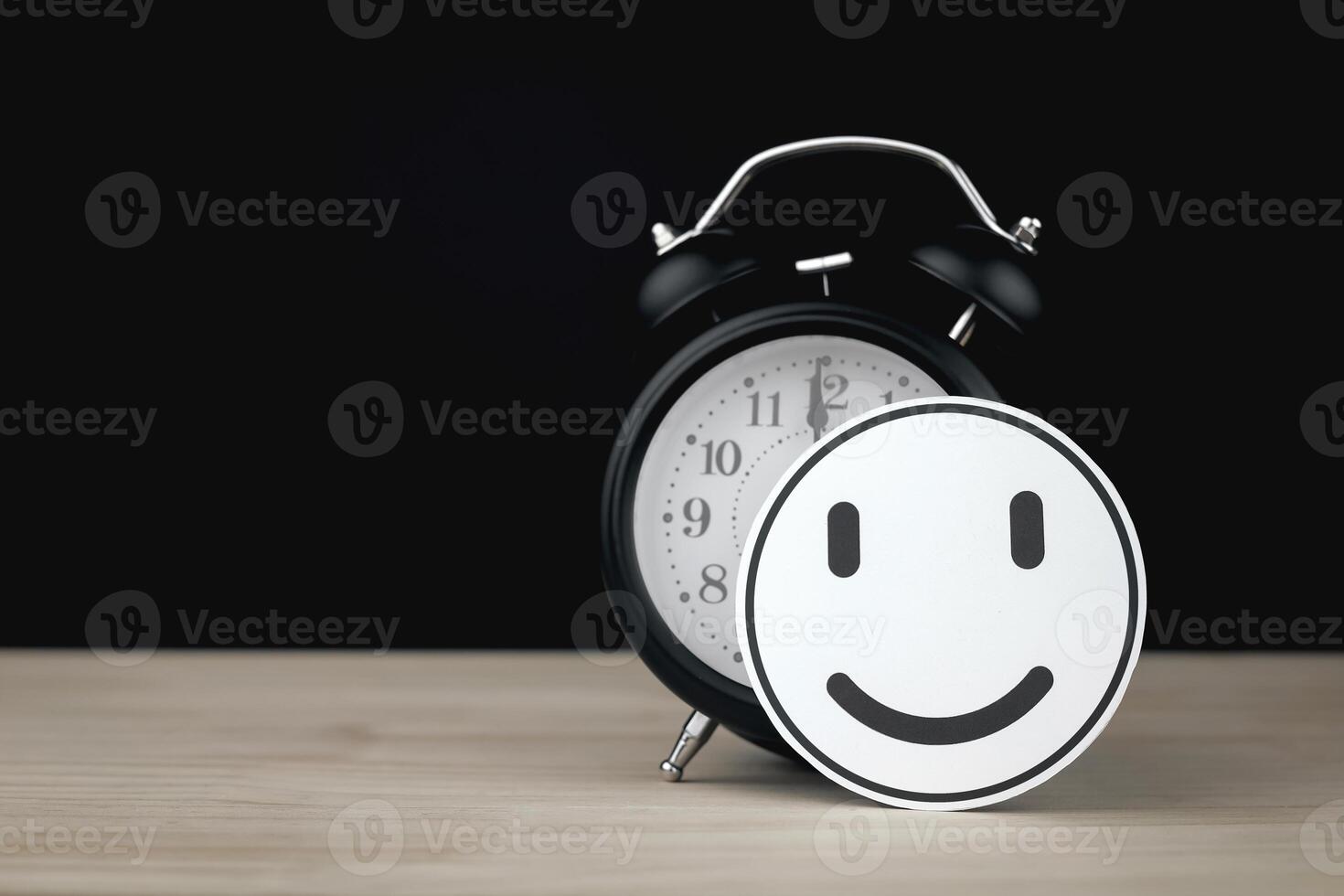 Circle paper with smiling face placed in front of black desk clock. with copy space, Concept of time management and efficient work time. photo