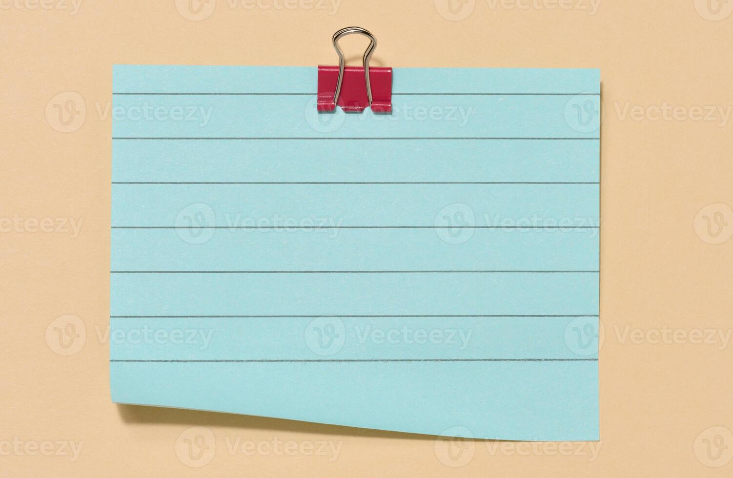 Blue sticky note secured with a red paper clip, centered on a beige background. photo