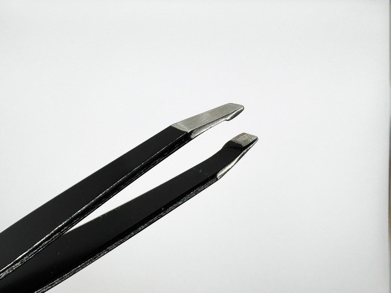 Black metal tweezers with a silver tip on a white background are on the left in the image photo