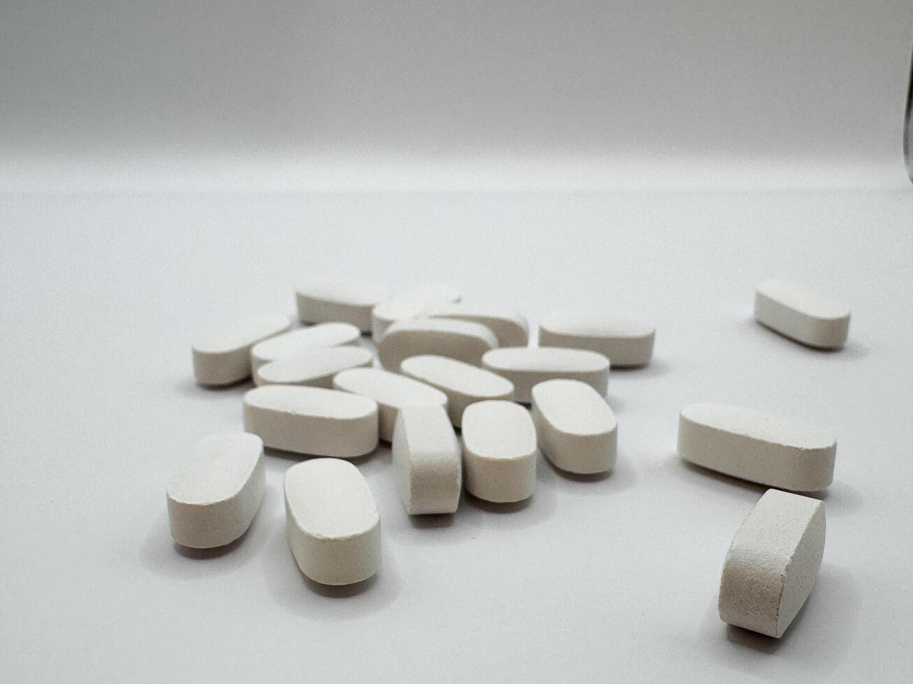 White pills for illness lie on a white background in a scattering and in a pile on the surface, front view photo