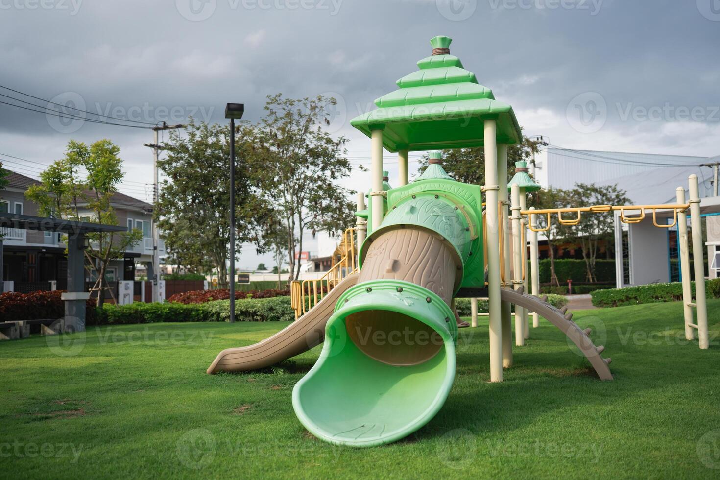 Vibrant Play Area with Green Slide and Tower in Outdoor Park Surrounded by Grass and Trees Under a Cloudy Sky photo