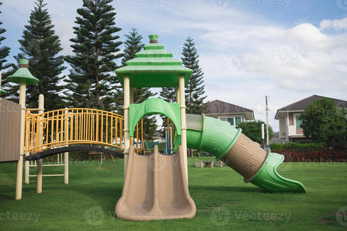 Colorful playground structure with slide and climbing area in a grassy park setting under a bright sky with trees in the background photo