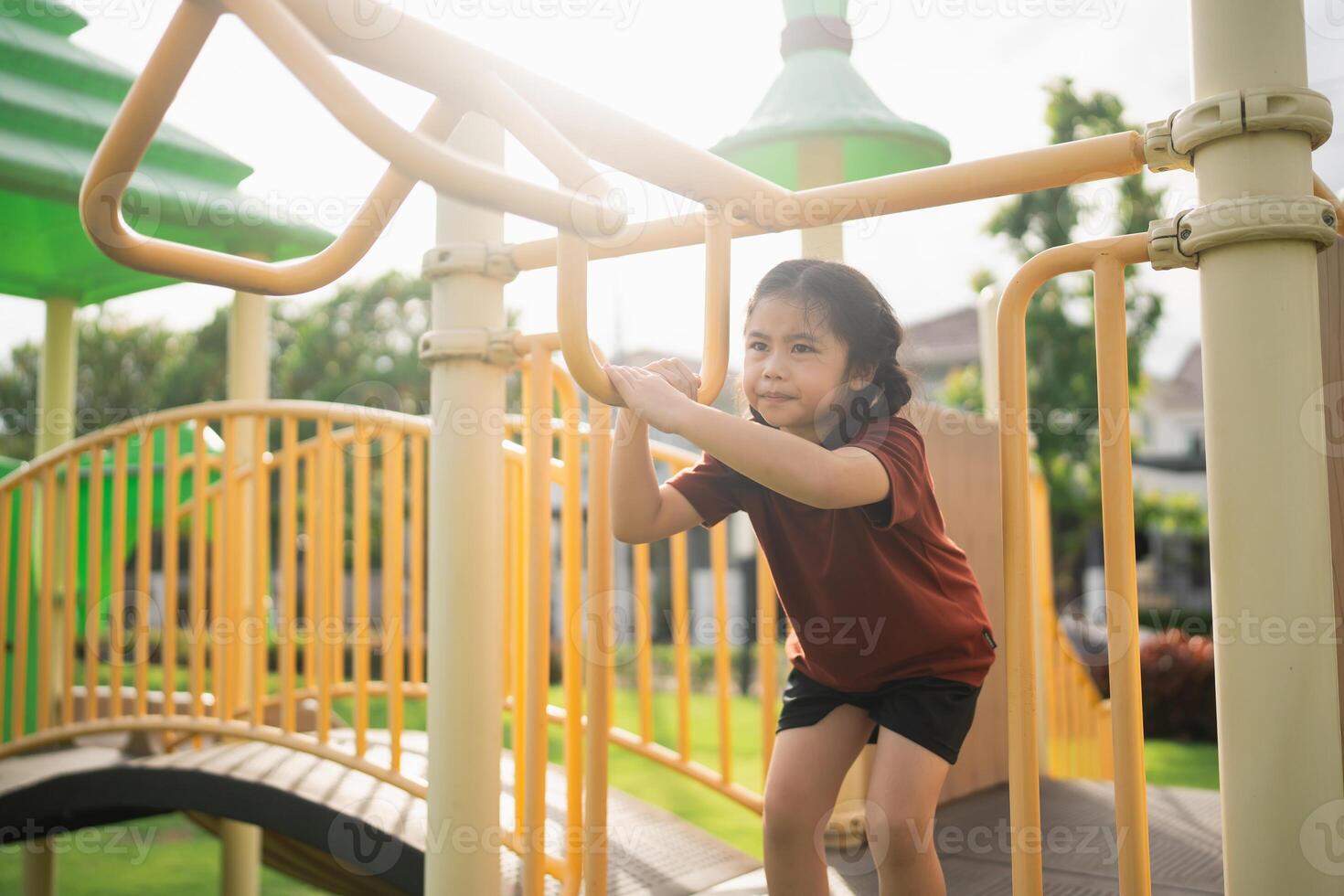 Young girl climbing playground equipment under bright sunlight enjoying outdoor activity in a vibrant park setting with green trees and playful environment photo