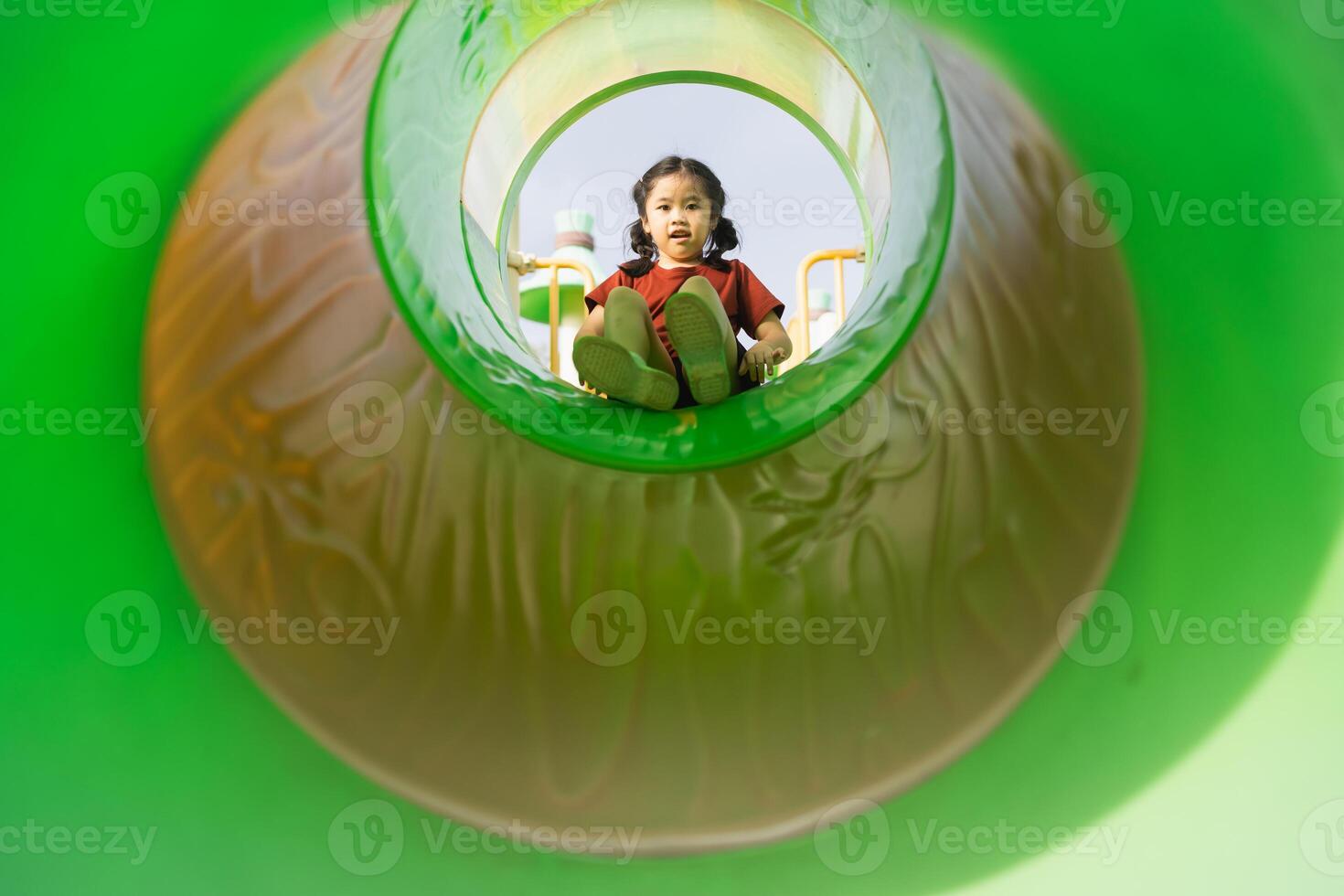 Joyful Child Playing in Colorful Playground Slide Captured from Inside Viewpoint with Bright Green Surroundings, Fun Outdoor Activity Daytime photo