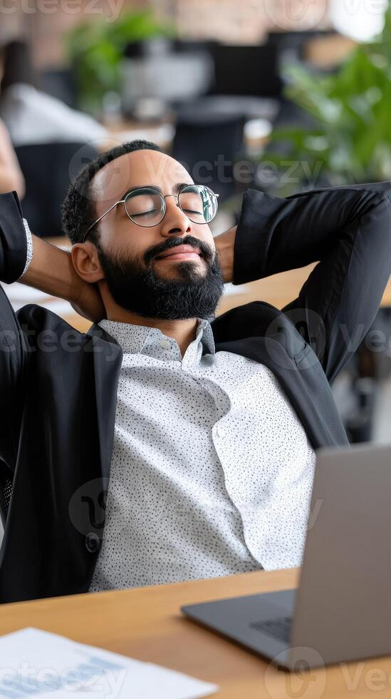 A man with glasses and a beard is relaxing in front of a laptop photo