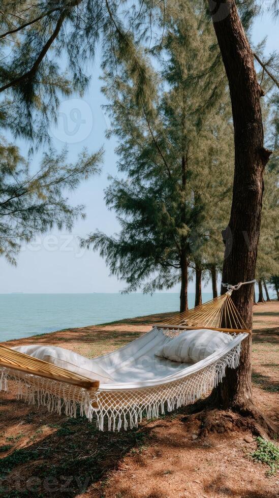 Hammock with fringes sways gently from a tree on a sunny beach, with the vibrant blue sea and sky in the background, perfect for relaxation and leisure photo
