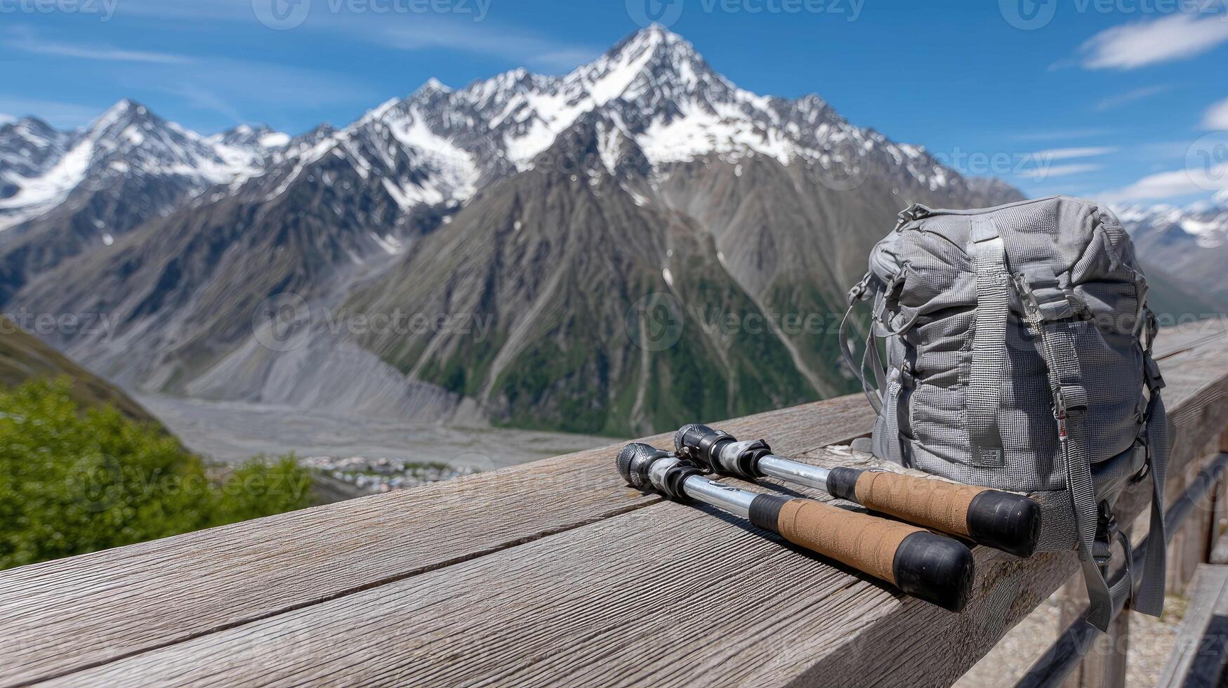 A backpack and two hiking poles sit on a wooden bench overlooking a mountain range photo
