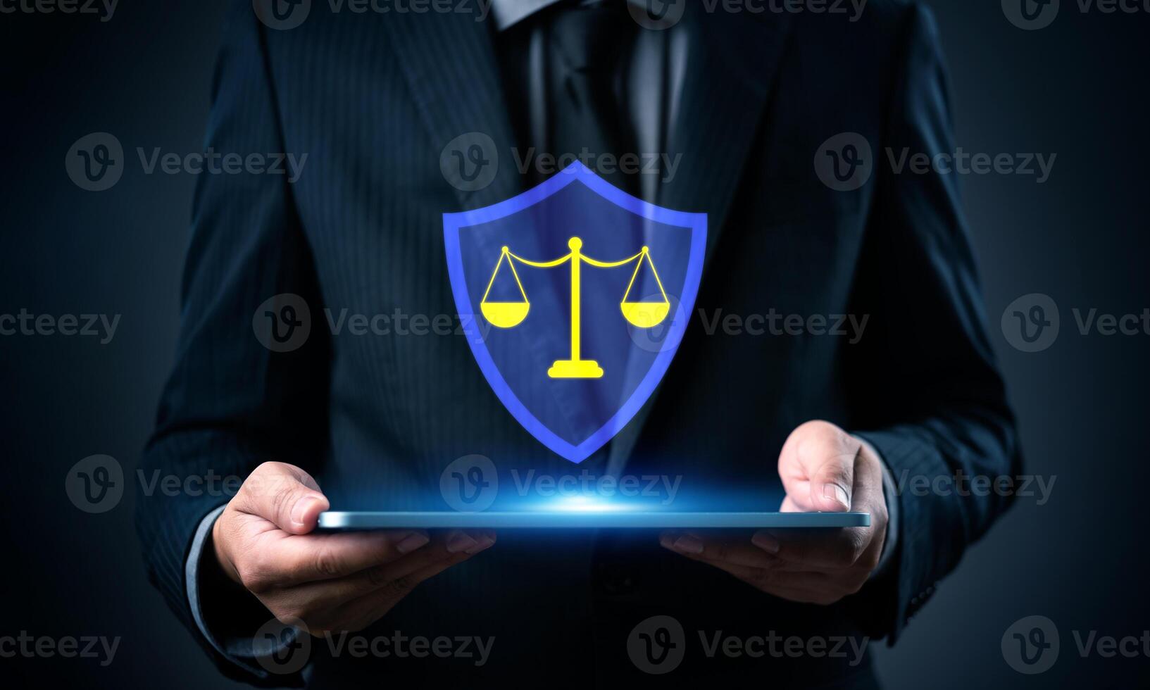 Businessman holding tablet with justice symbol on dark background photo