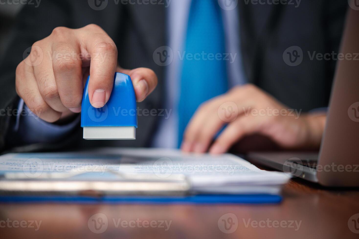 A person in a suit holding a blue rubber stamp photo
