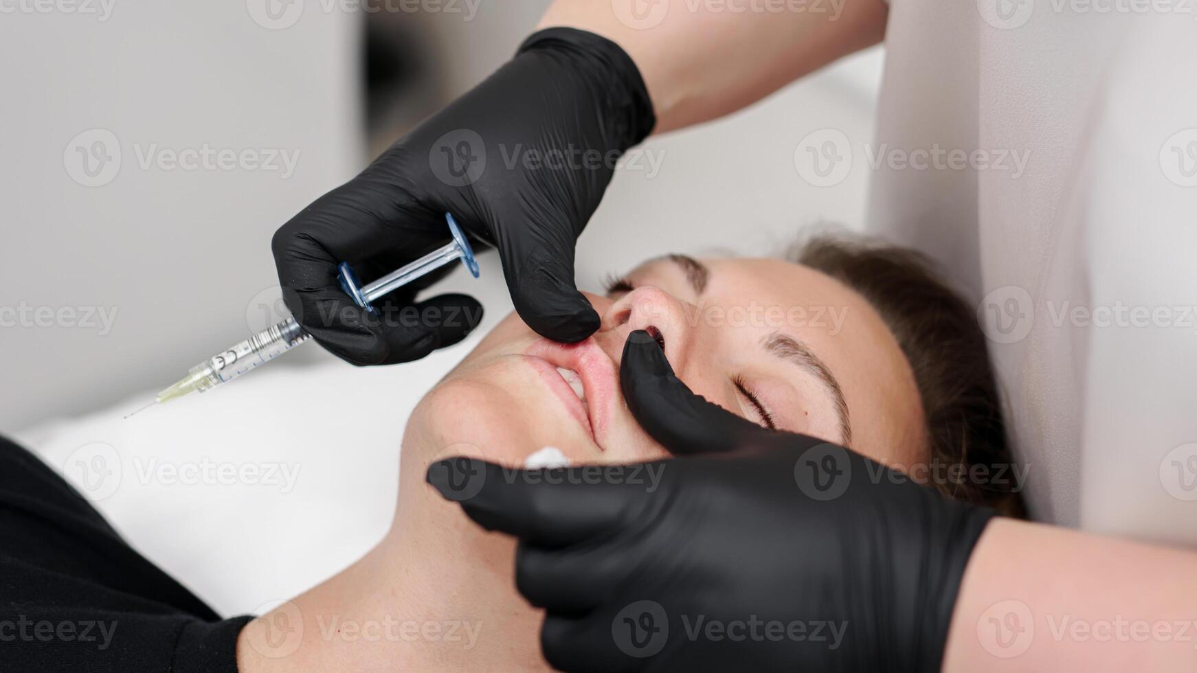 A specialist gives an injection into the lips of a young woman. Lip augmentation and correction procedure. Cosmetology concept. photo