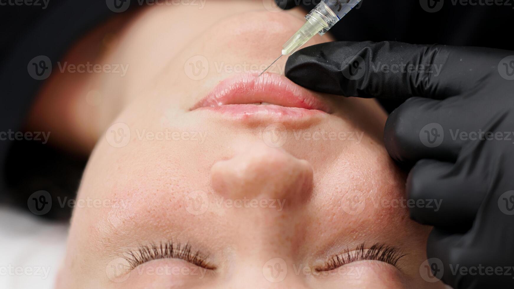 A beautician injects filler into the lips of a young woman. Lip augmentation injection procedure. Advertising concept for facial care, youth and beauty. photo