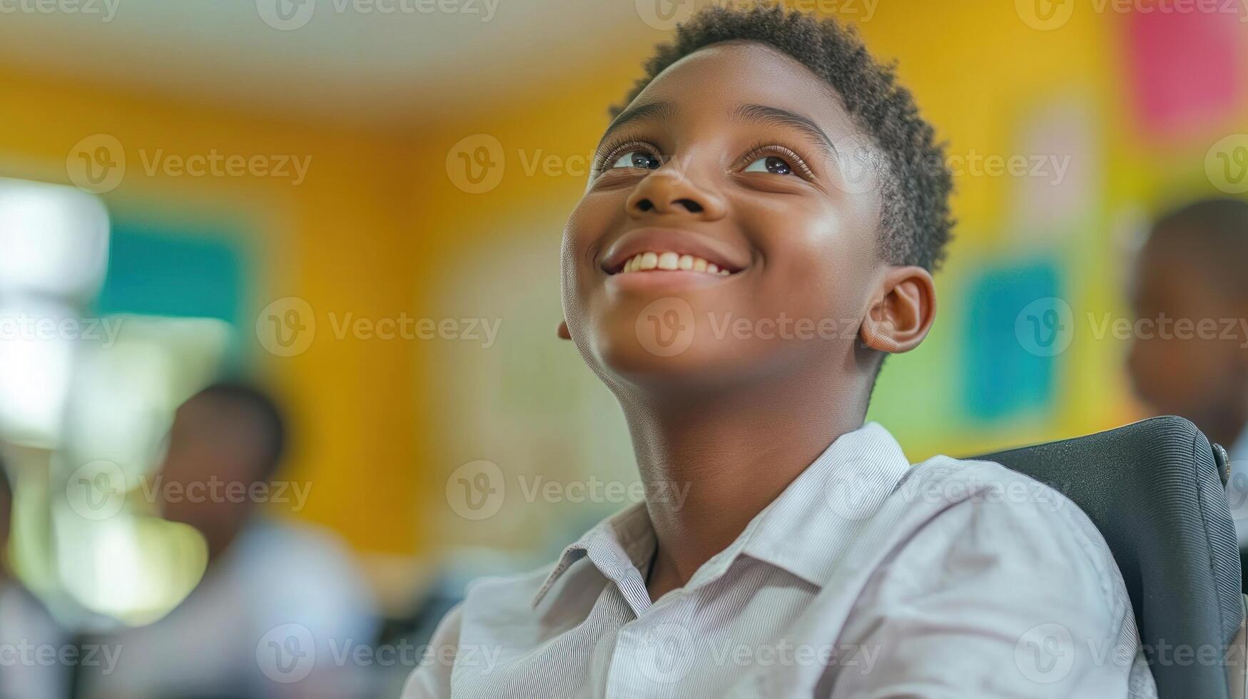 A young boy smiles while sitting in a classroom photo