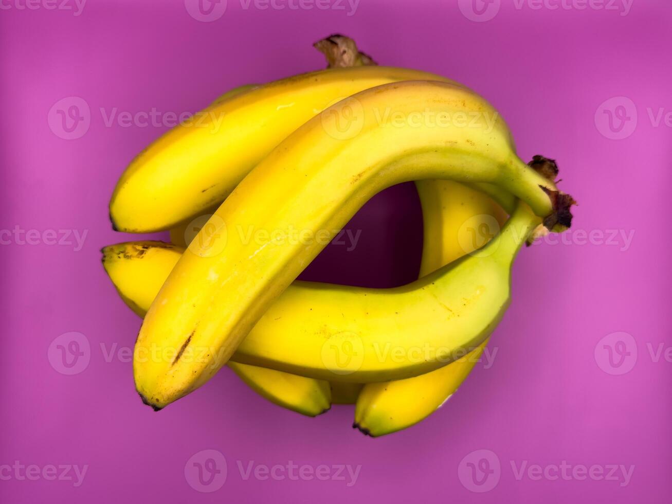 Jenga game of eight bright yellow bananas lying on purple background, top view, center of image photo