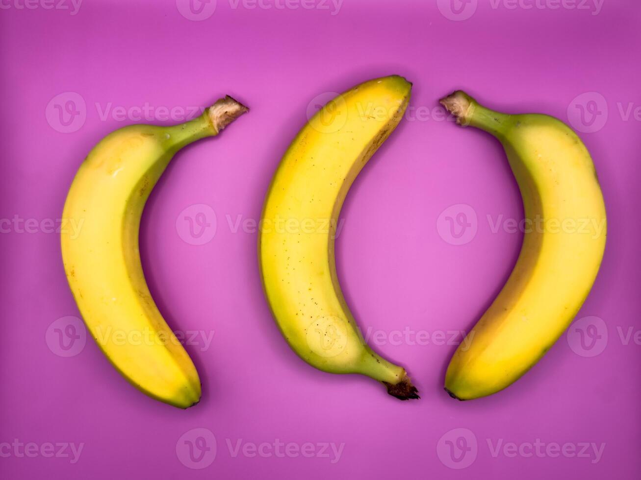 Three bright yellow bananas lie on a purple background, top view photo