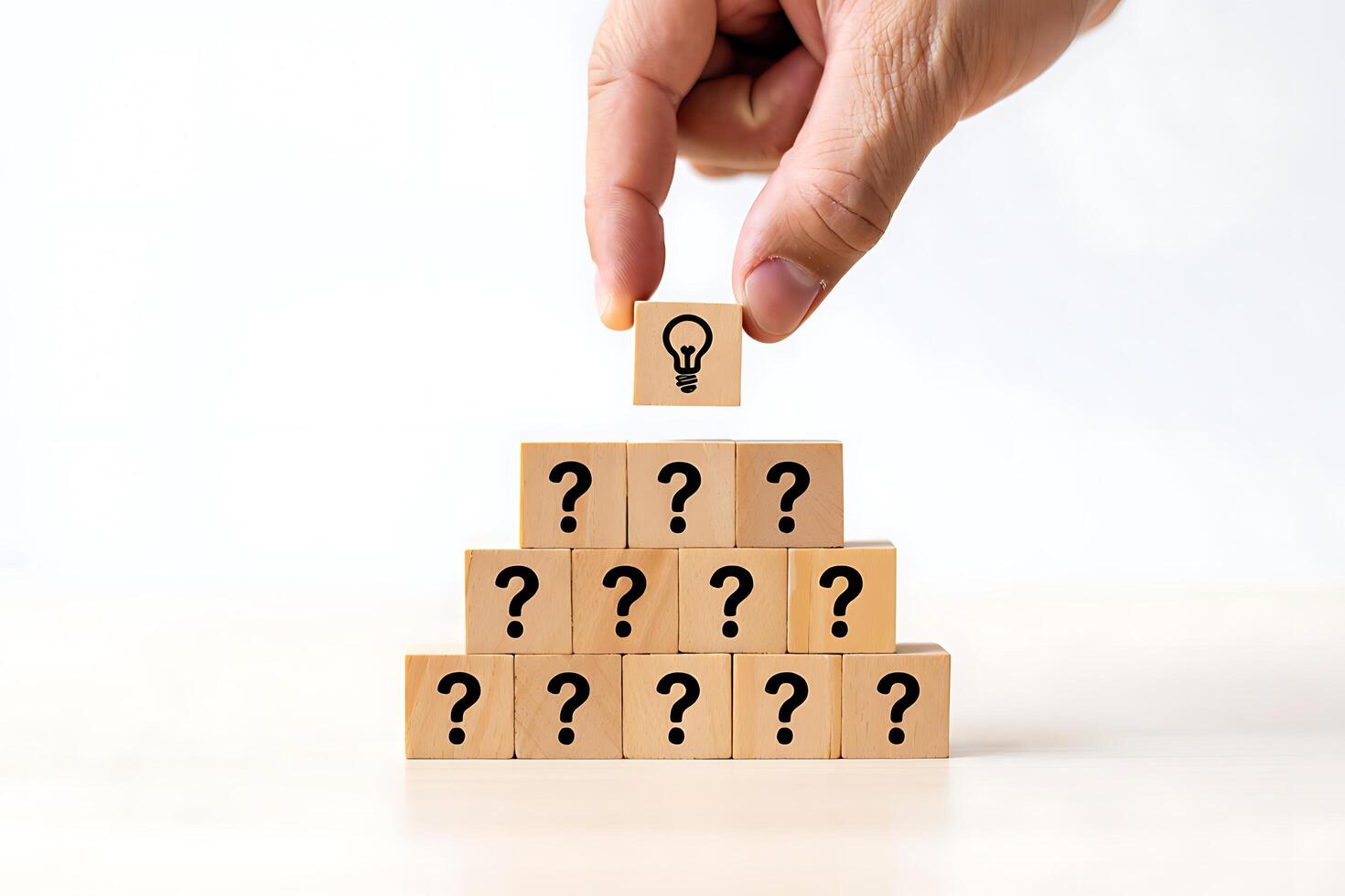 Hand places lightbulb block on pyramid of question mark blocks symbolizing idea generation photo