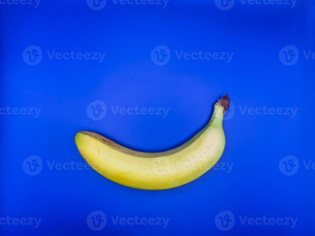 A bright yellow banana lies on a bright blue background at the bottom of the image, top view photo