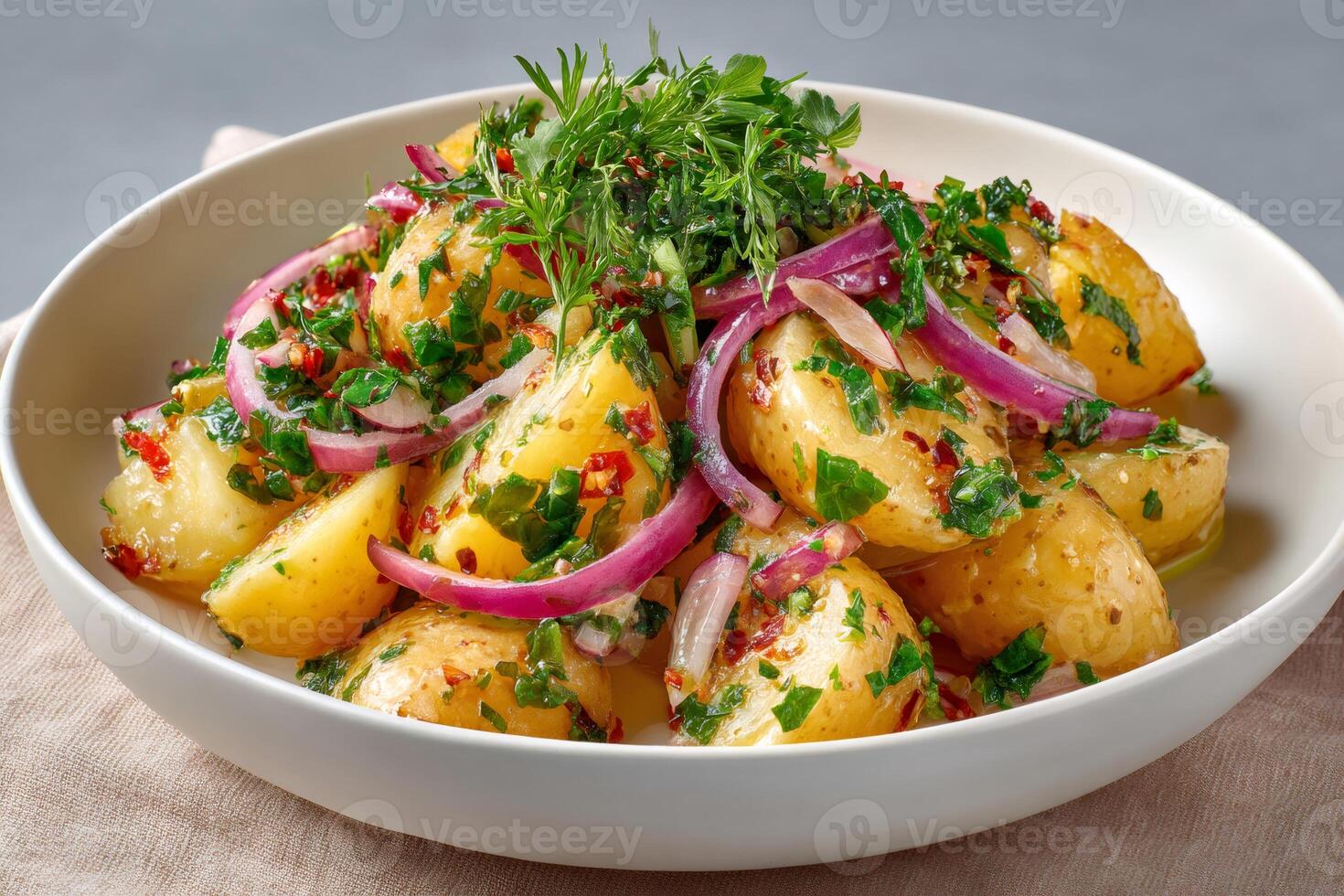 Warm potato salad with red onion, fresh dill and parsley resting in a white bowl photo