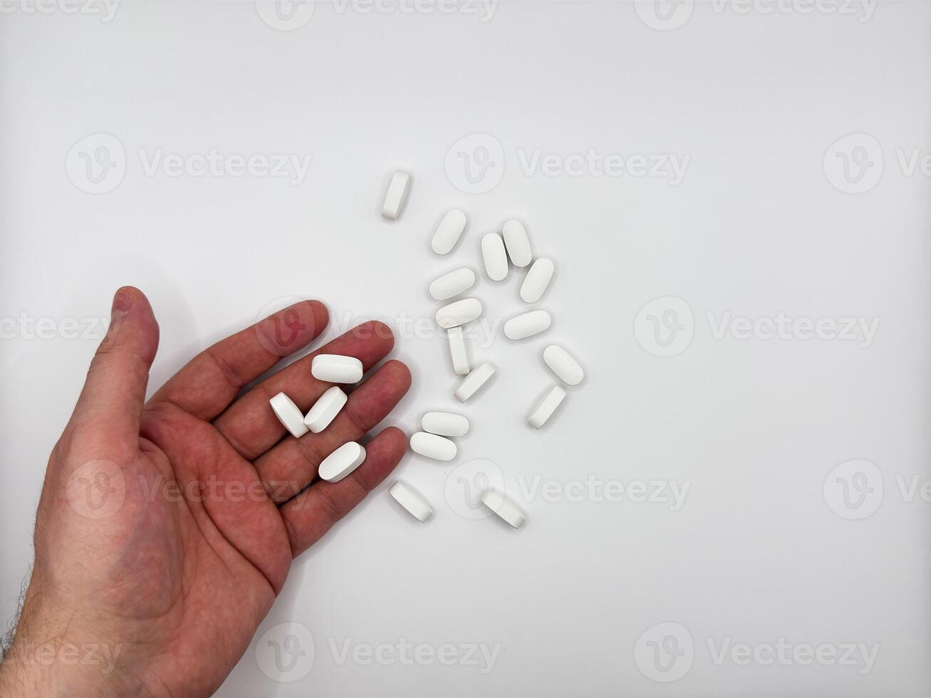 White pills for illness fell out of a man's hand in a pile on a white background, hand on the left in the image top view photo