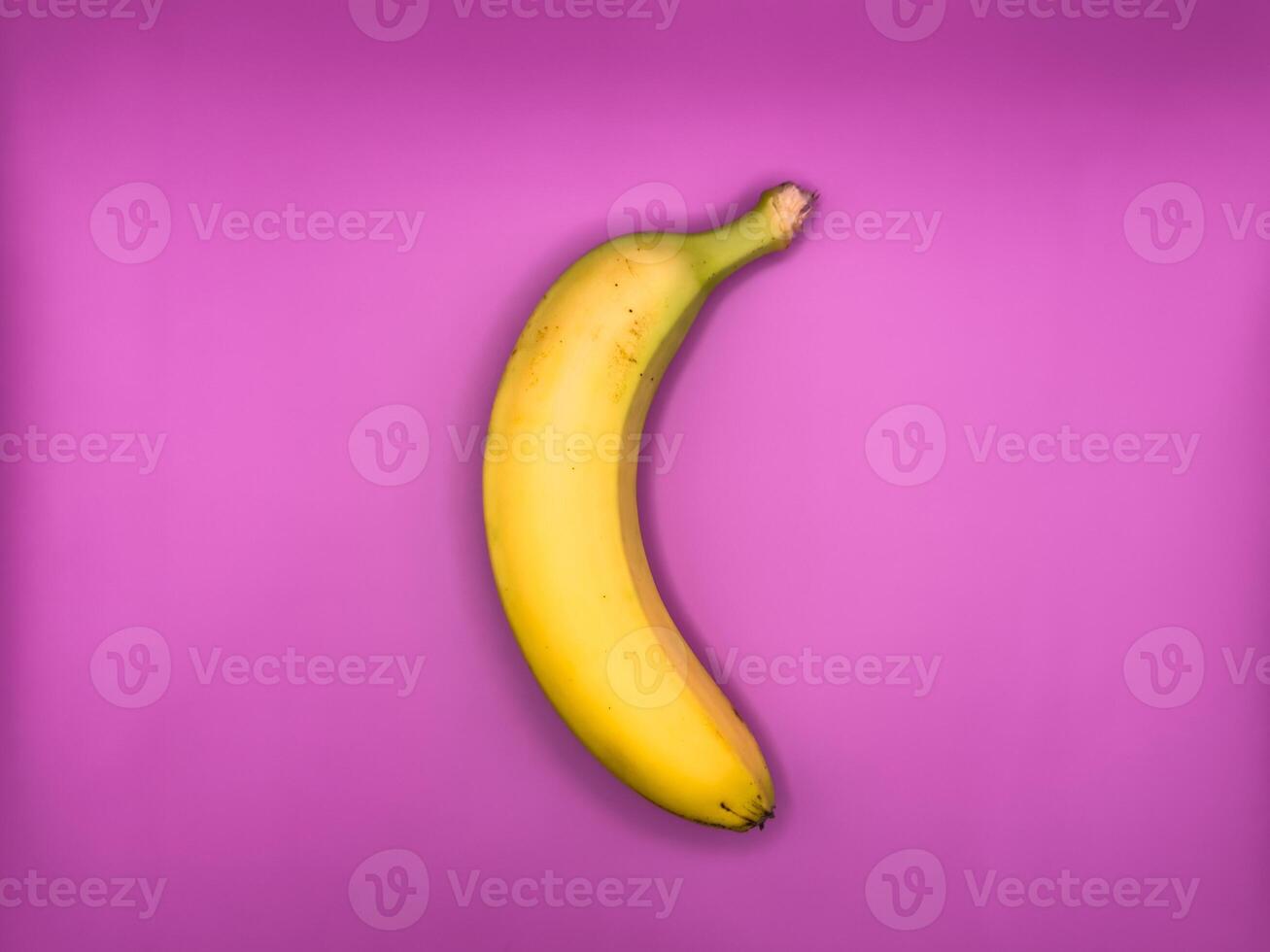 One bright yellow banana lies vertically on a purple background, top view, center of the image photo