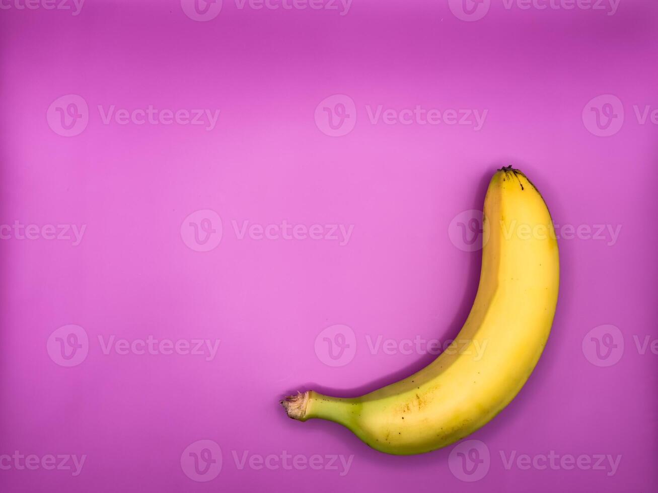 A bright yellow banana lies on a purple background on the bottom right, top view photo