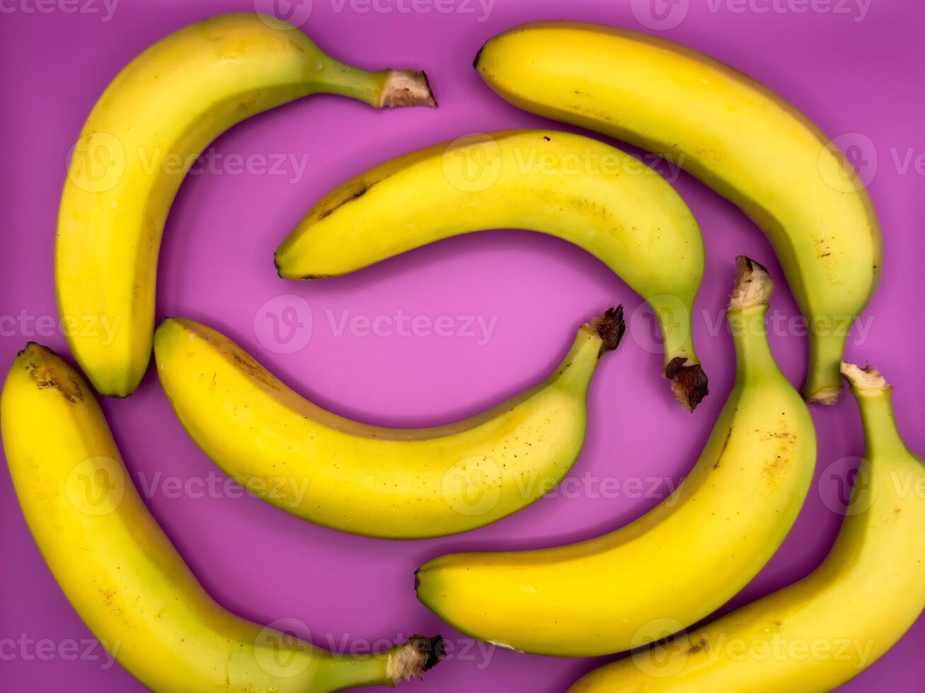 Background of bright yellow bananas lie on a purple background, top view, centered in the image photo