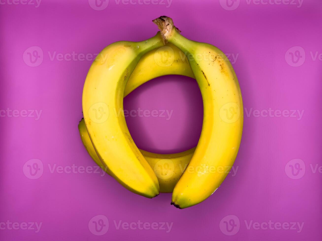 Jenga game of four bright yellow bananas lying on purple background, top view, center of image photo