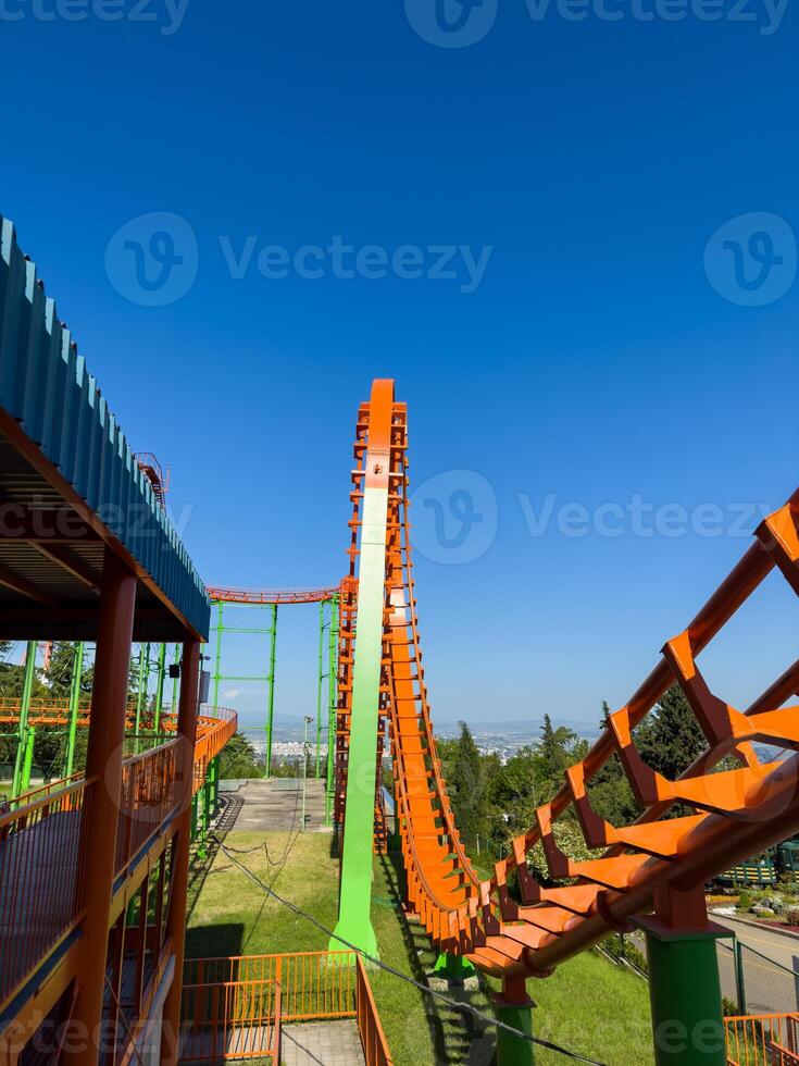 Orange roller coaster at an amusement park with cloudy blue sky, vertical photo for social media, copy space
