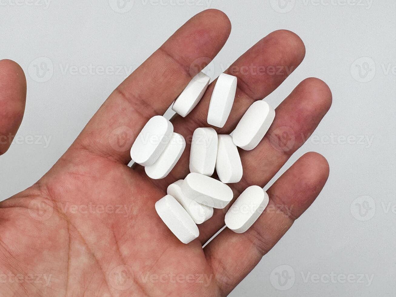 White pills for illness lie in a man's hand on a white background, hand on the left in the image top view photo