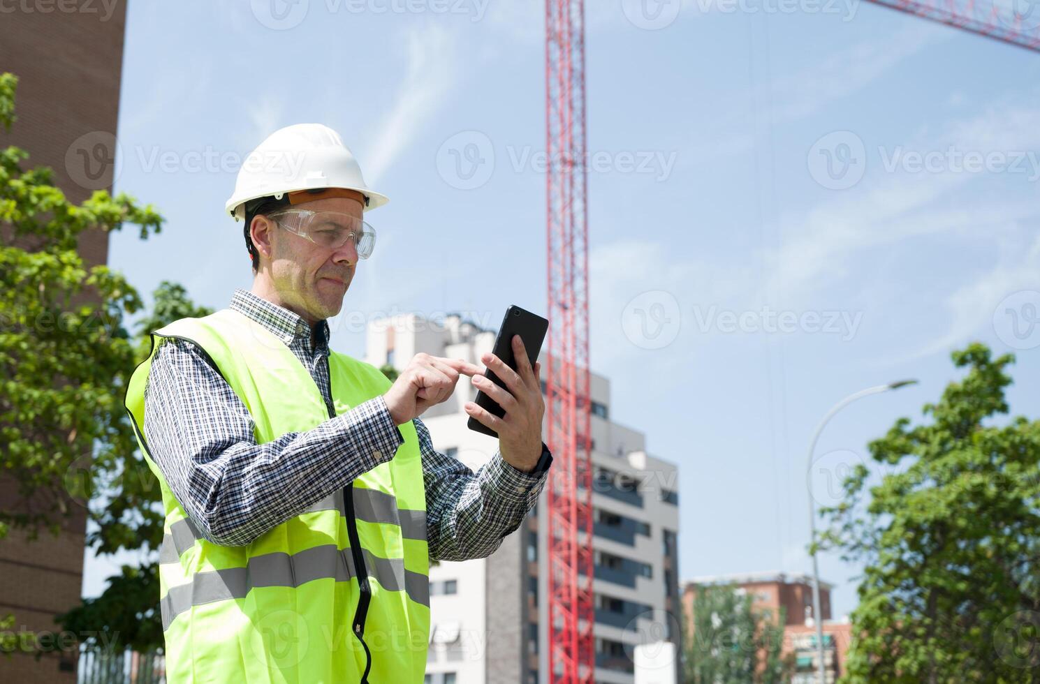 Professional male construction worker with safety helmet and reflective vest and safety glasses at a construction site with building progress.. photo