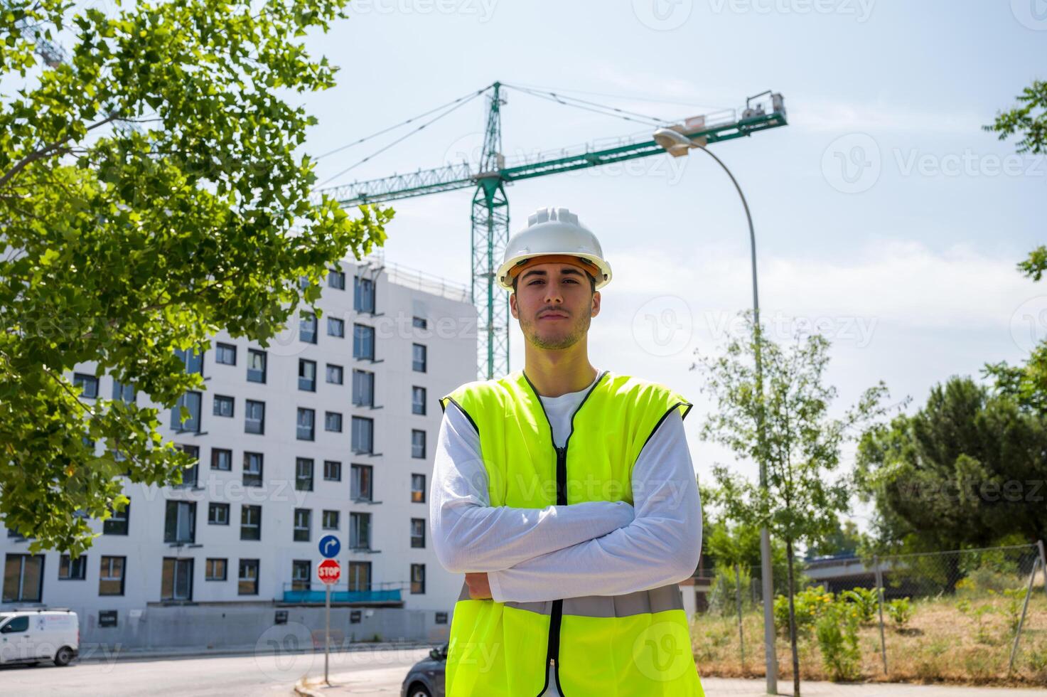 Professional young male construction worker with safety helmet and reflective vest at a construction site with building progress in the background, photo